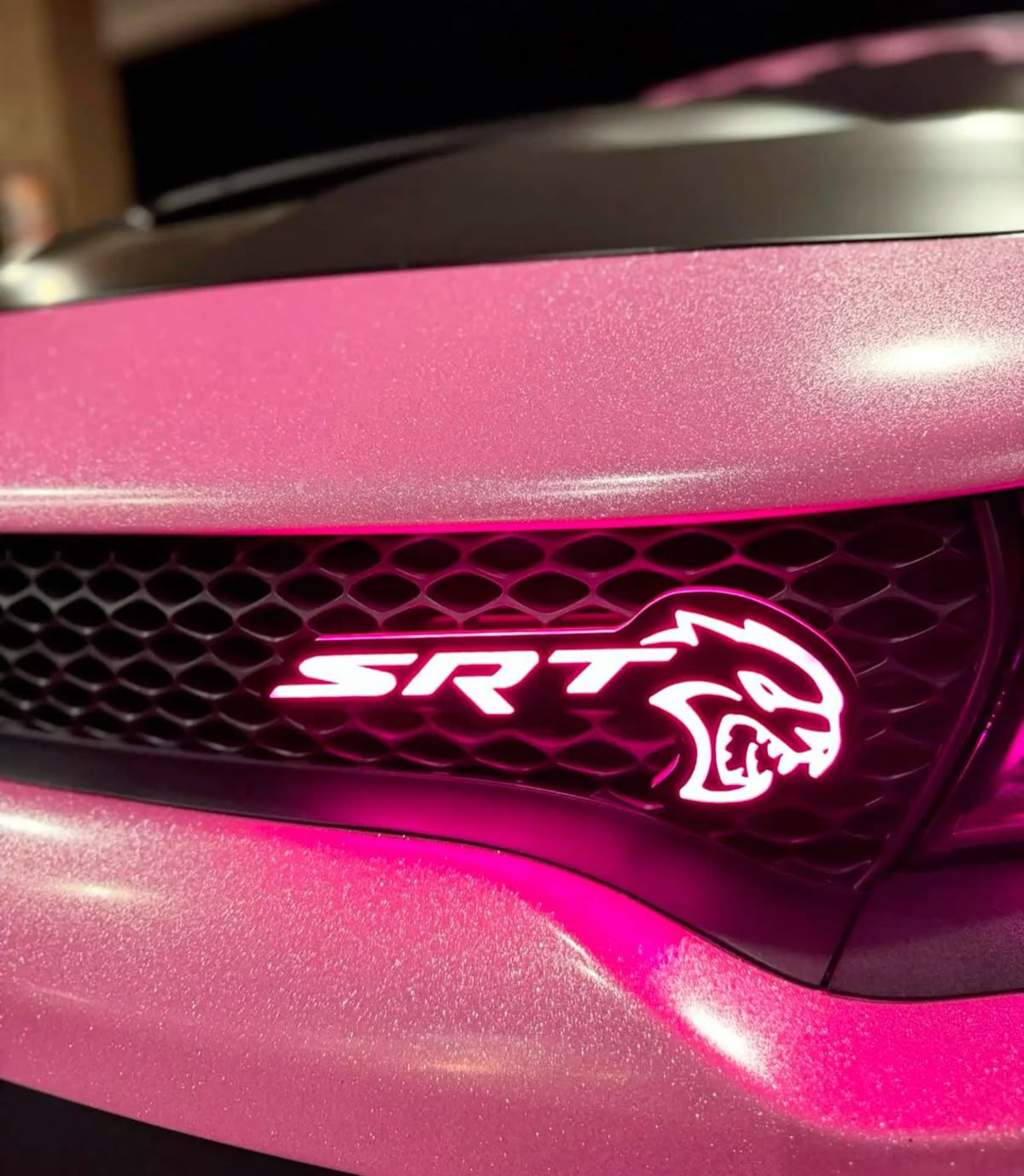 AutoJeweler SRT Hellcat RGB Flow Series emblem installed on a pink Dodge Charger grille close up glowing pink.
