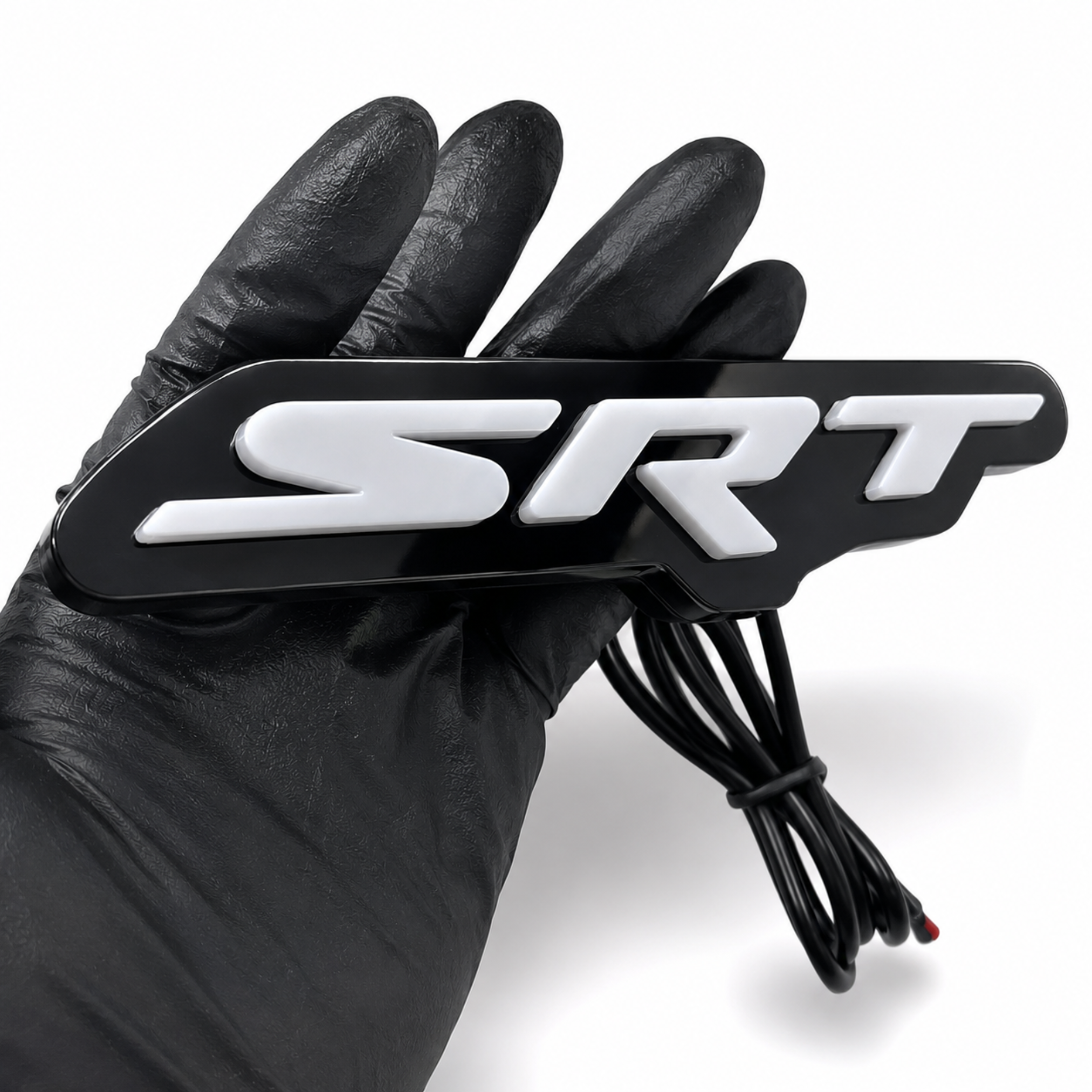 Close-up of SRT LED emblem badge showing raised 3D white acrylic letters, gloss black faceplate, and wiring lead