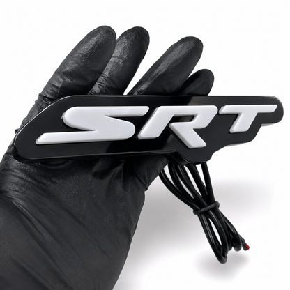Close-up of SRT LED emblem badge showing raised 3D white acrylic letters, gloss black faceplate, and wiring lead