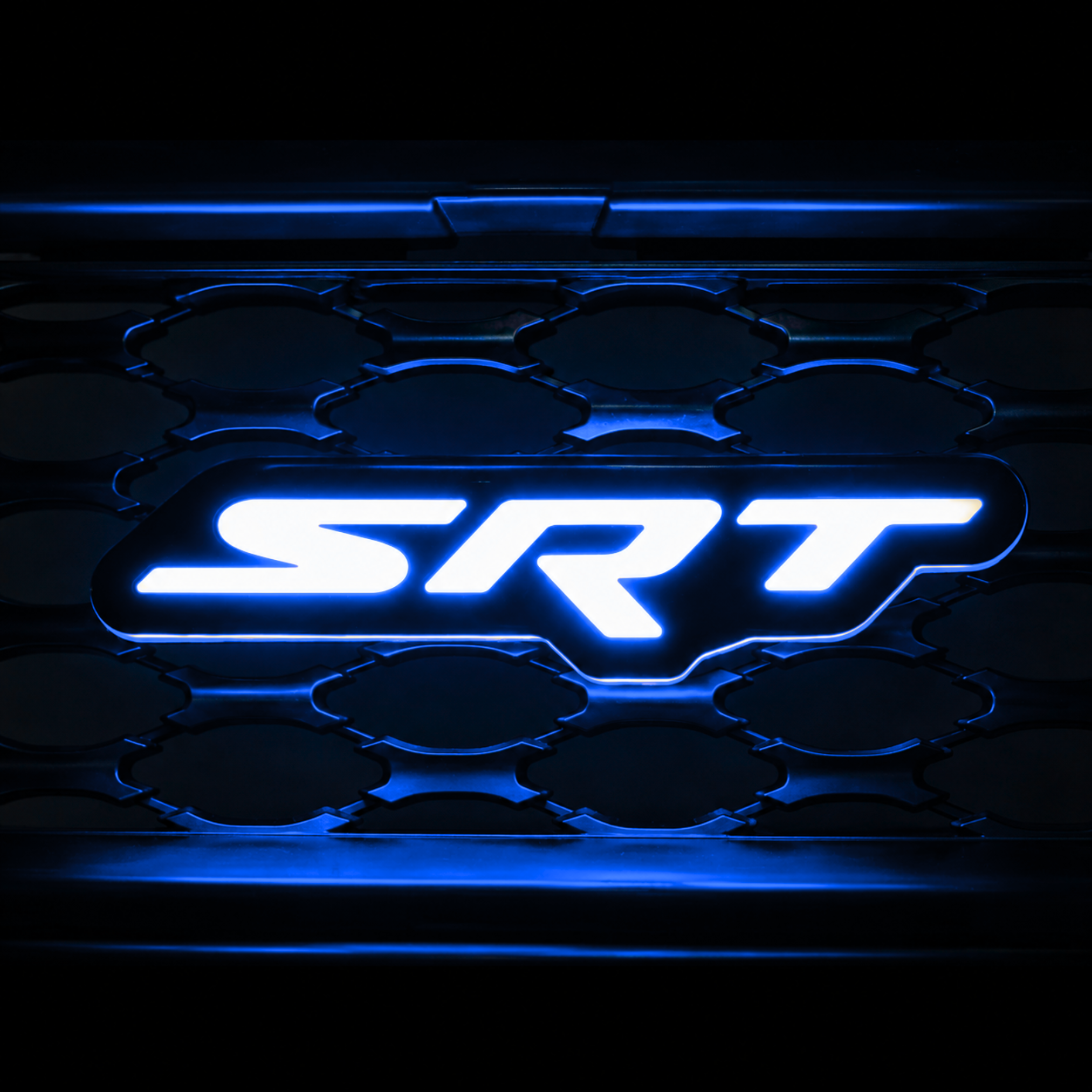 SRT LED grille emblem installed on black grille illuminated in blue with matching blue glow and grille reflections.